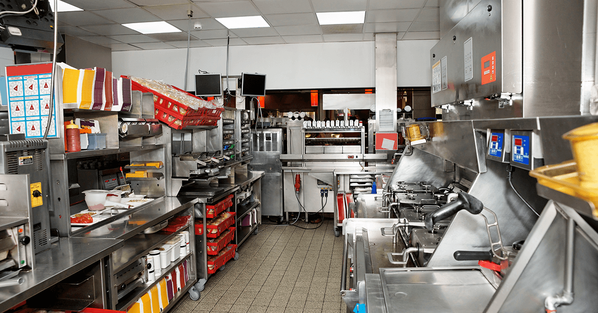 Photo shows a fast food restaurant kitchen, including metal counters, cooking appliances, and restaurant technology like the kitchen display system